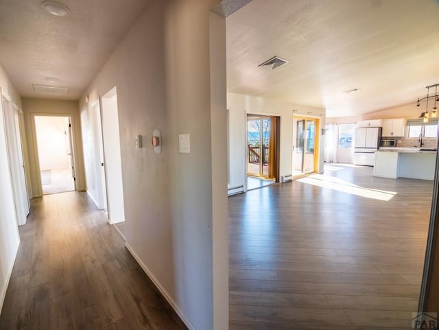 hall with baseboards, visible vents, baseboard heating, and dark wood-type flooring