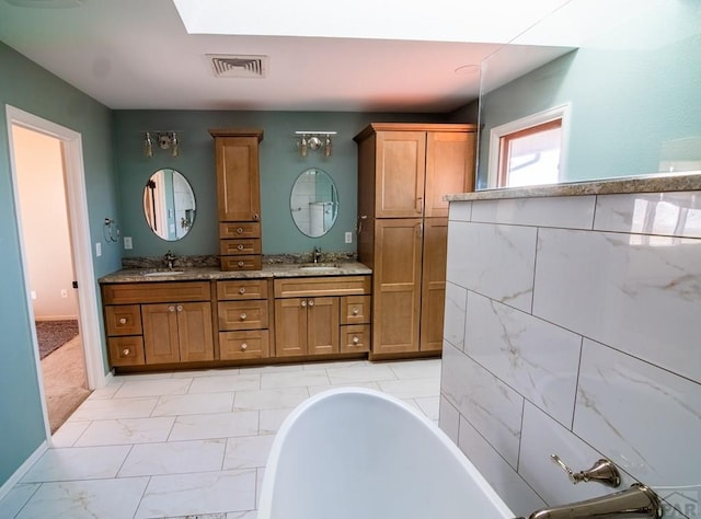 full bathroom with marble finish floor, a soaking tub, a sink, and visible vents