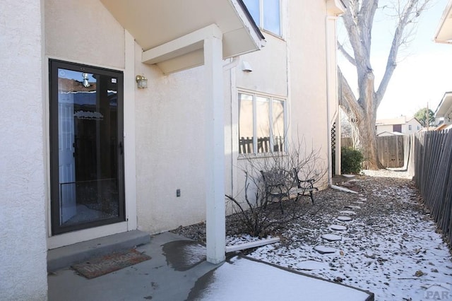 snow covered property entrance featuring fence and stucco siding