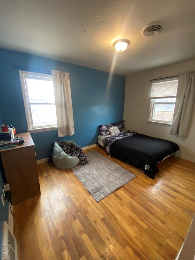 bedroom with multiple windows, light wood-type flooring, visible vents, and baseboards