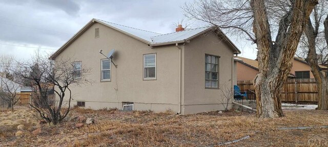 view of property exterior with metal roof, fence, and stucco siding