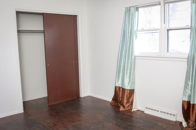 unfurnished bedroom with a baseboard radiator, a closet, baseboards, and wood finished floors