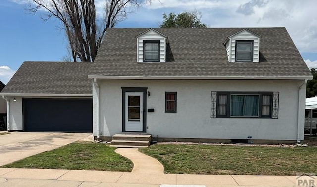 new england style home with an attached garage, a front yard, concrete driveway, and roof with shingles