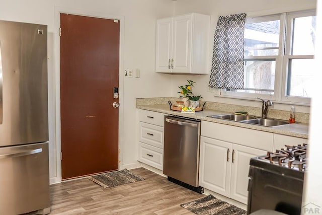 kitchen with stainless steel appliances, a sink, white cabinets, light countertops, and light wood-type flooring