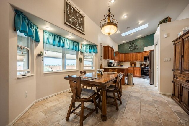 dining space with light tile patterned floors, vaulted ceiling with skylight, and baseboards