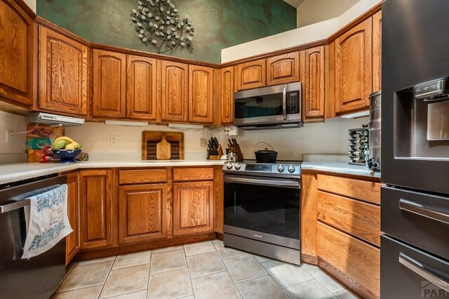 kitchen featuring light tile patterned floors, light countertops, appliances with stainless steel finishes, and brown cabinets