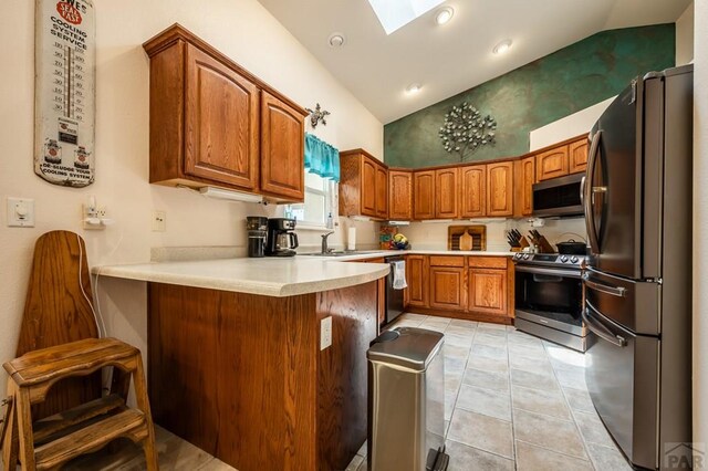 kitchen featuring a peninsula, a skylight, light countertops, appliances with stainless steel finishes, and brown cabinets