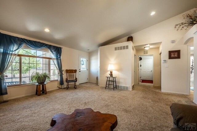 living area featuring arched walkways, visible vents, vaulted ceiling, and light carpet