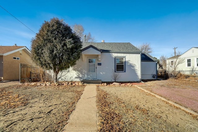 bungalow-style house featuring roof with shingles, fence, and stucco siding