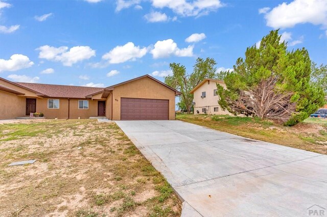 single story home featuring a garage, concrete driveway, a front lawn, and stucco siding