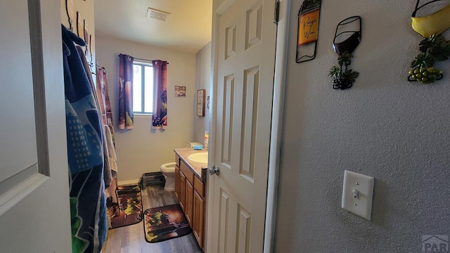 full bath featuring toilet, wood finished floors, visible vents, vanity, and baseboards