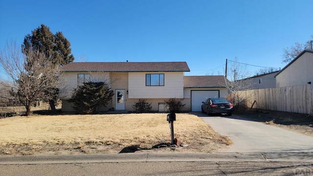 raised ranch featuring an attached garage, fence, concrete driveway, and brick siding