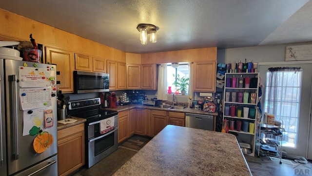 kitchen featuring a textured ceiling, appliances with stainless steel finishes, dark wood-style flooring, and a sink