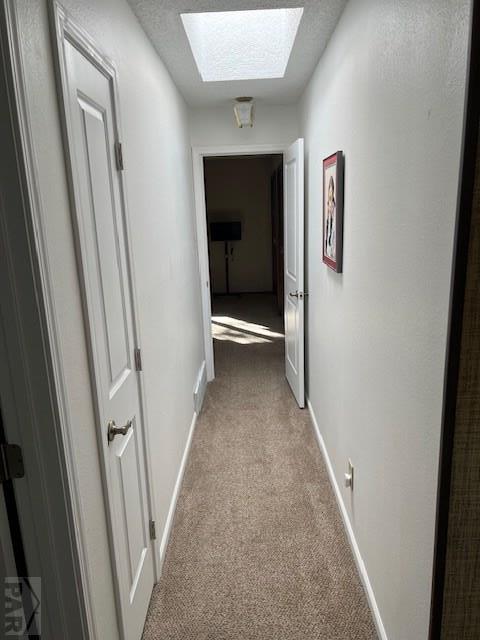 hallway featuring a skylight, light colored carpet, a textured ceiling, and baseboards