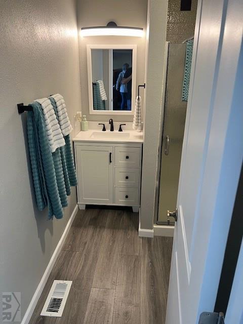 full bath with wood finished floors, vanity, visible vents, baseboards, and a stall shower