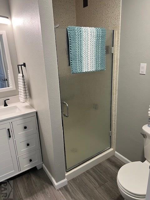 bathroom featuring toilet, wood finished floors, vanity, baseboards, and a stall shower