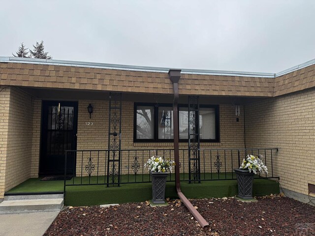 doorway to property with roof with shingles, mansard roof, and brick siding