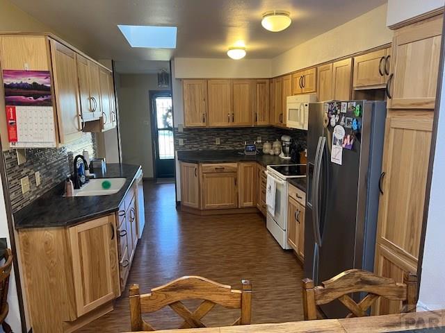 kitchen featuring a sink, white appliances, dark countertops, and a skylight