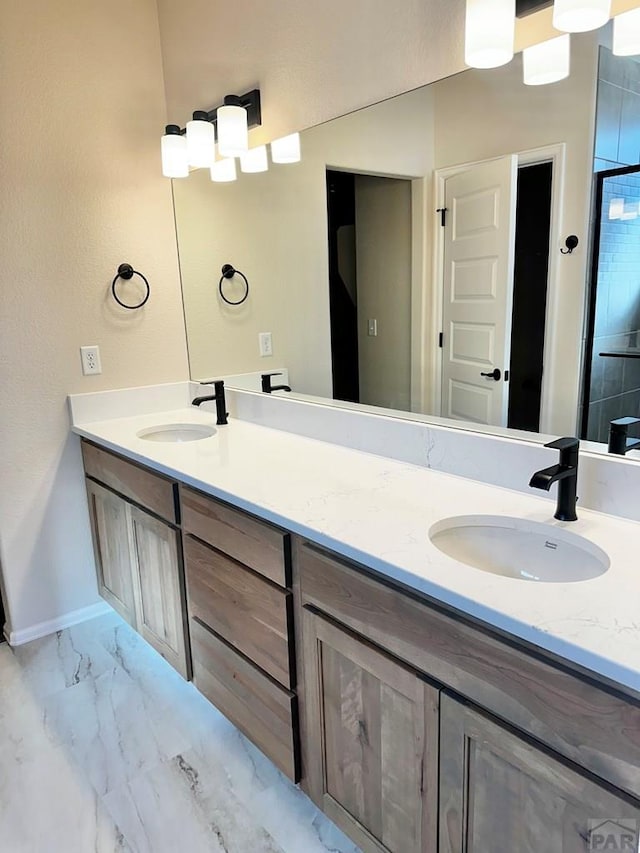 bathroom with marble finish floor, double vanity, a sink, and baseboards