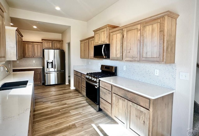 kitchen with stainless steel appliances, a sink, light wood-type flooring, light stone countertops, and tasteful backsplash