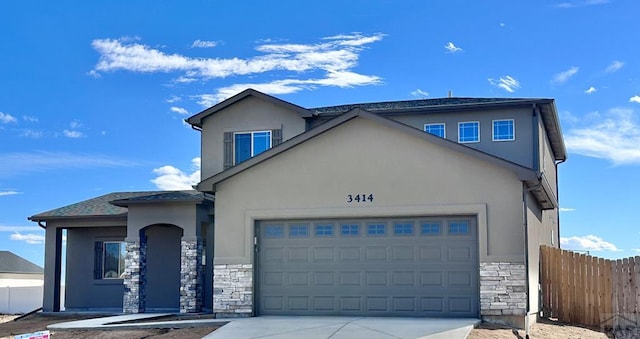 view of front of house featuring a garage, stone siding, fence, and stucco siding