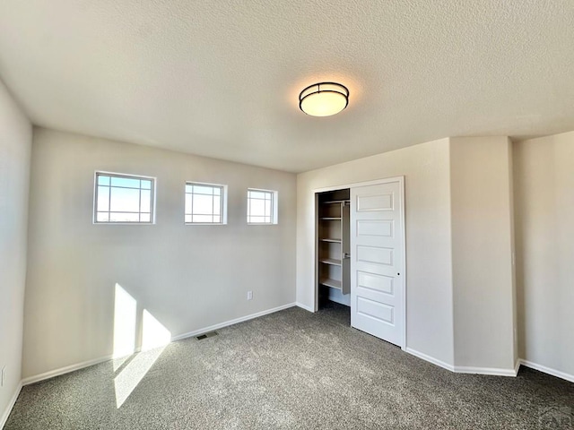 unfurnished bedroom with baseboards, visible vents, dark colored carpet, a textured ceiling, and a closet