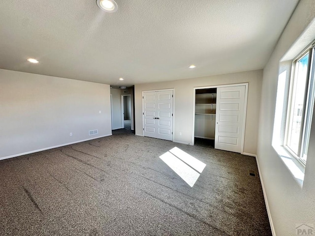 unfurnished bedroom with baseboards, visible vents, dark carpet, and multiple closets