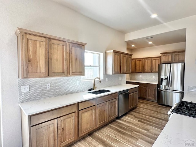 kitchen featuring a sink, appliances with stainless steel finishes, backsplash, brown cabinets, and dark wood finished floors