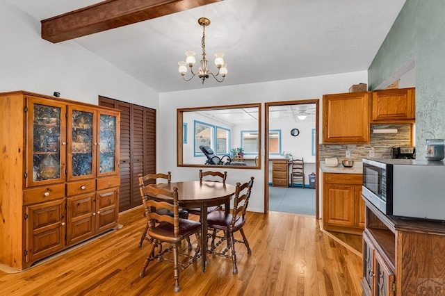 dining area featuring light wood-style floors, a notable chandelier, and vaulted ceiling with beams