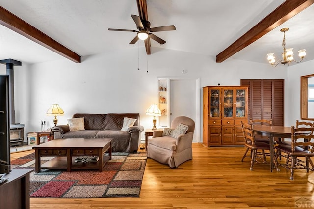 living room featuring ceiling fan with notable chandelier, beamed ceiling, wood finished floors, and a wood stove