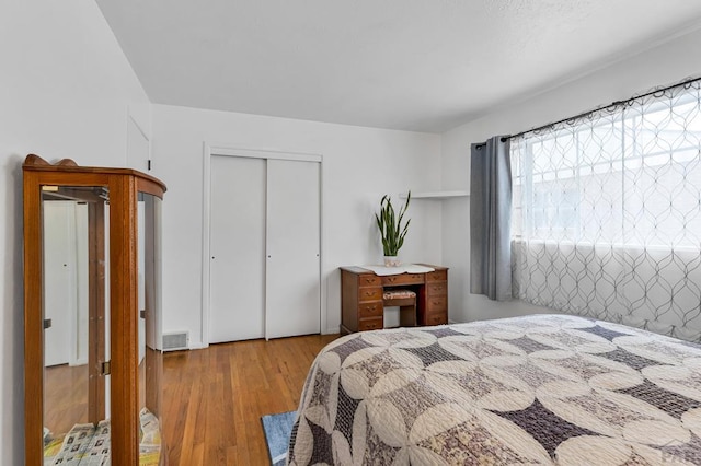 bedroom with light wood finished floors, visible vents, and a closet