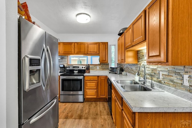 kitchen with brown cabinetry, stainless steel appliances, light countertops, light wood-style floors, and a sink