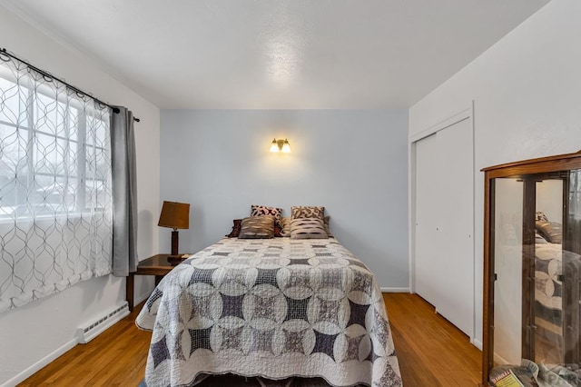 bedroom featuring light wood-style floors, baseboards, a baseboard heating unit, and a closet