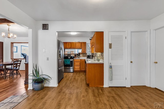 kitchen featuring pendant lighting, brown cabinets, light countertops, appliances with stainless steel finishes, and a sink