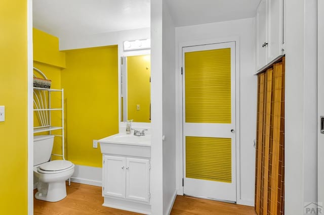 bathroom with toilet, wood finished floors, vanity, and baseboards