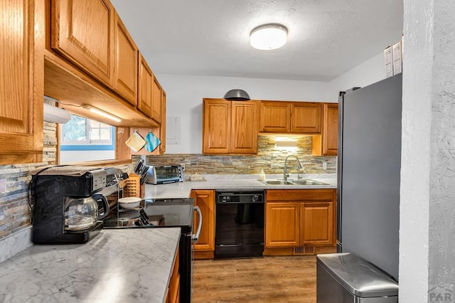 kitchen with light countertops, brown cabinetry, freestanding refrigerator, a sink, and dishwasher