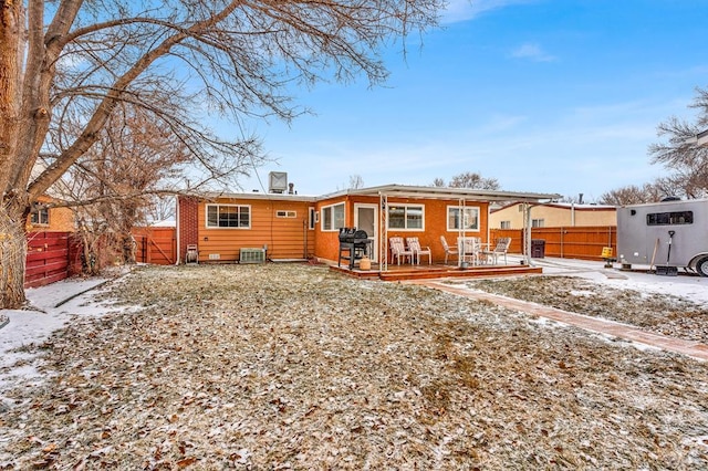 snow covered back of property with cooling unit, fence, and a deck