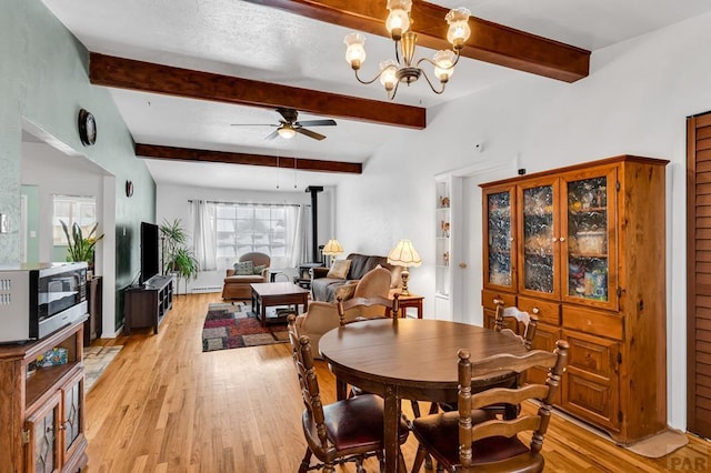 dining space with a wood stove, light wood-type flooring, beam ceiling, and ceiling fan with notable chandelier