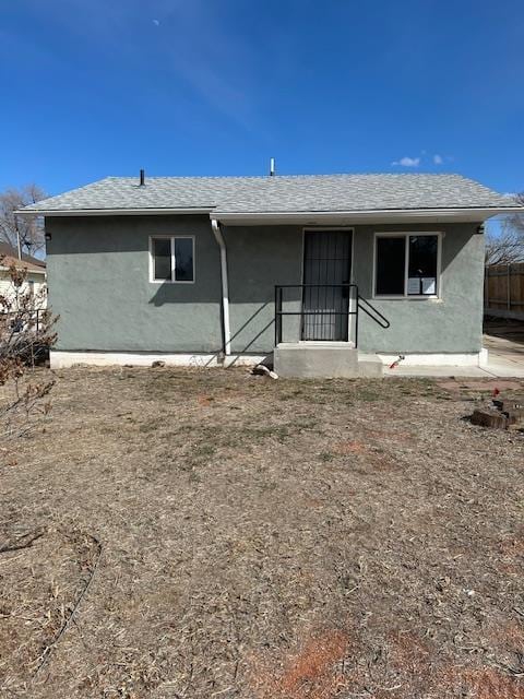 rear view of house with stucco siding, roof with shingles, and fence