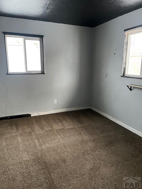 spare room featuring a textured ceiling, baseboards, and dark colored carpet