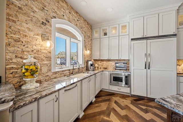 kitchen with glass insert cabinets, white cabinets, a sink, and built in appliances