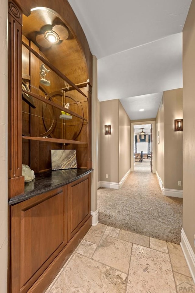 hallway featuring light carpet, baseboards, and stone tile flooring