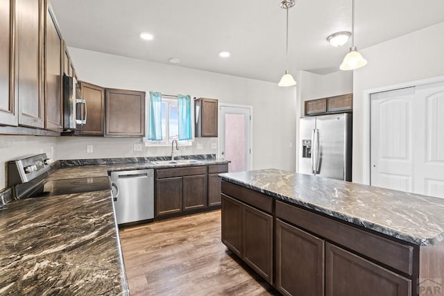 kitchen featuring appliances with stainless steel finishes, a center island, hanging light fixtures, light wood-style floors, and a sink