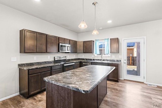 kitchen featuring dark brown cabinetry, a sink, appliances with stainless steel finishes, a center island, and decorative light fixtures