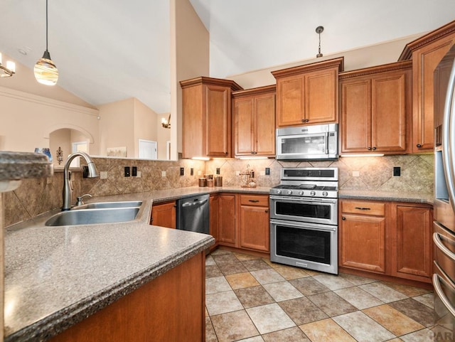 406 N Idledale Dr, Pueblo West, CO 81007 - kitchen featuring stainless steel appliances, vaulted ceiling, brown cabinetry, backsplash, and hanging light fixtures