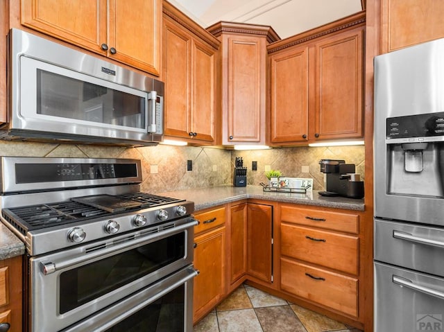 406 N Idledale Dr, Pueblo West, CO 81007 - kitchen featuring appliances with stainless steel finishes, tasteful backsplash, brown cabinetry, and dark stone counters