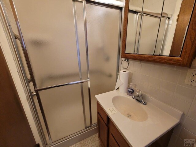 bathroom with tasteful backsplash, tile walls, vanity, and an enclosed shower