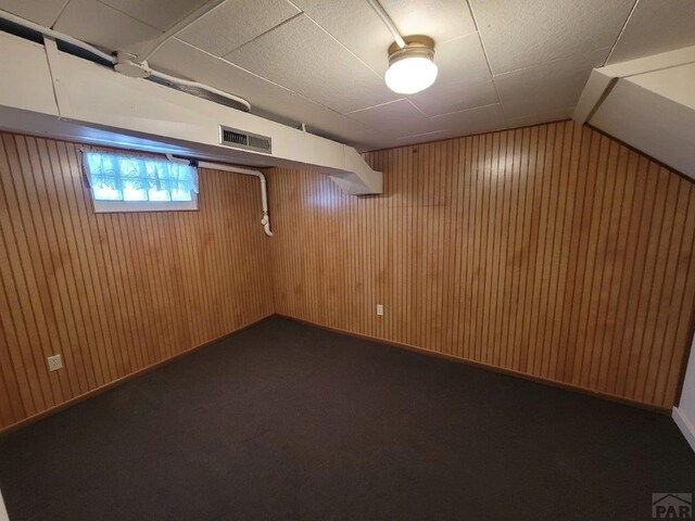 below grade area featuring wood walls, visible vents, and dark carpet