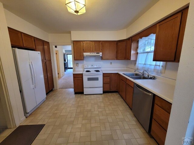 kitchen with white appliances, under cabinet range hood, light countertops, and a sink