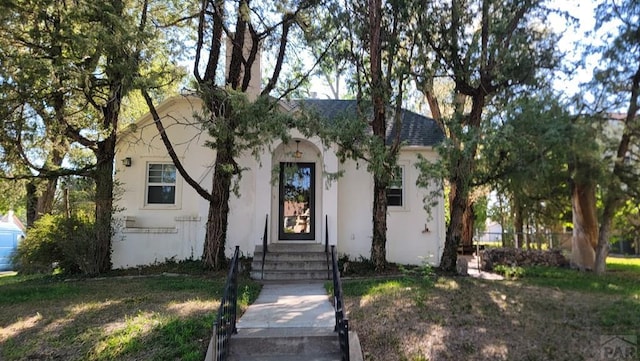 view of front facade featuring entry steps, stucco siding, roof with shingles, and a front yard